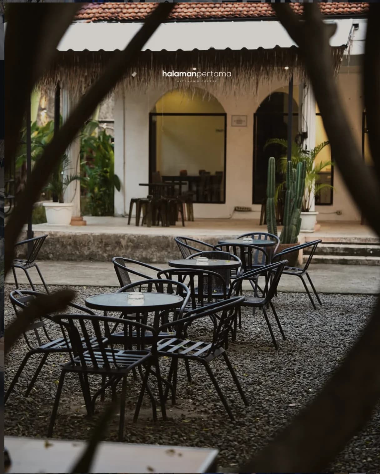 Area courtyard Halaman Pertama dengan meja, kursi, tanaman, dan bangunan berwarna hangat